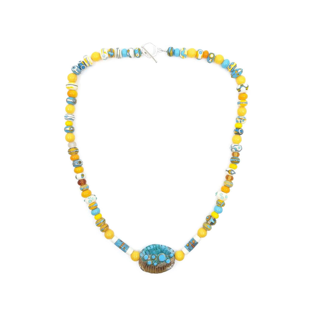 Full view of a yellow and turquoise glass bead necklace featuring alternating round and patterned beads with a large oval turquoise and brown focal bead at the center on a white background.