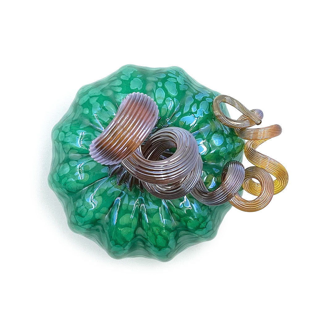 Top view of a green decorative glass pumpkin showing its textured marbled surface and spiraling amber, brown, and lavender stem.