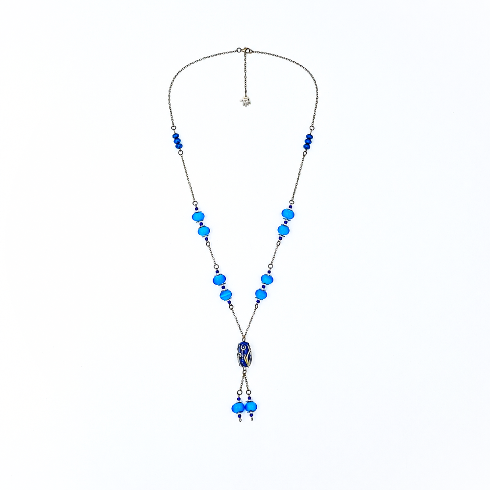 Wide view of a handmade blue lariat necklace featuring antique-bronze chain, bright blue glass beads, a decorative deep blue focal bead, and two dangling bead drops.