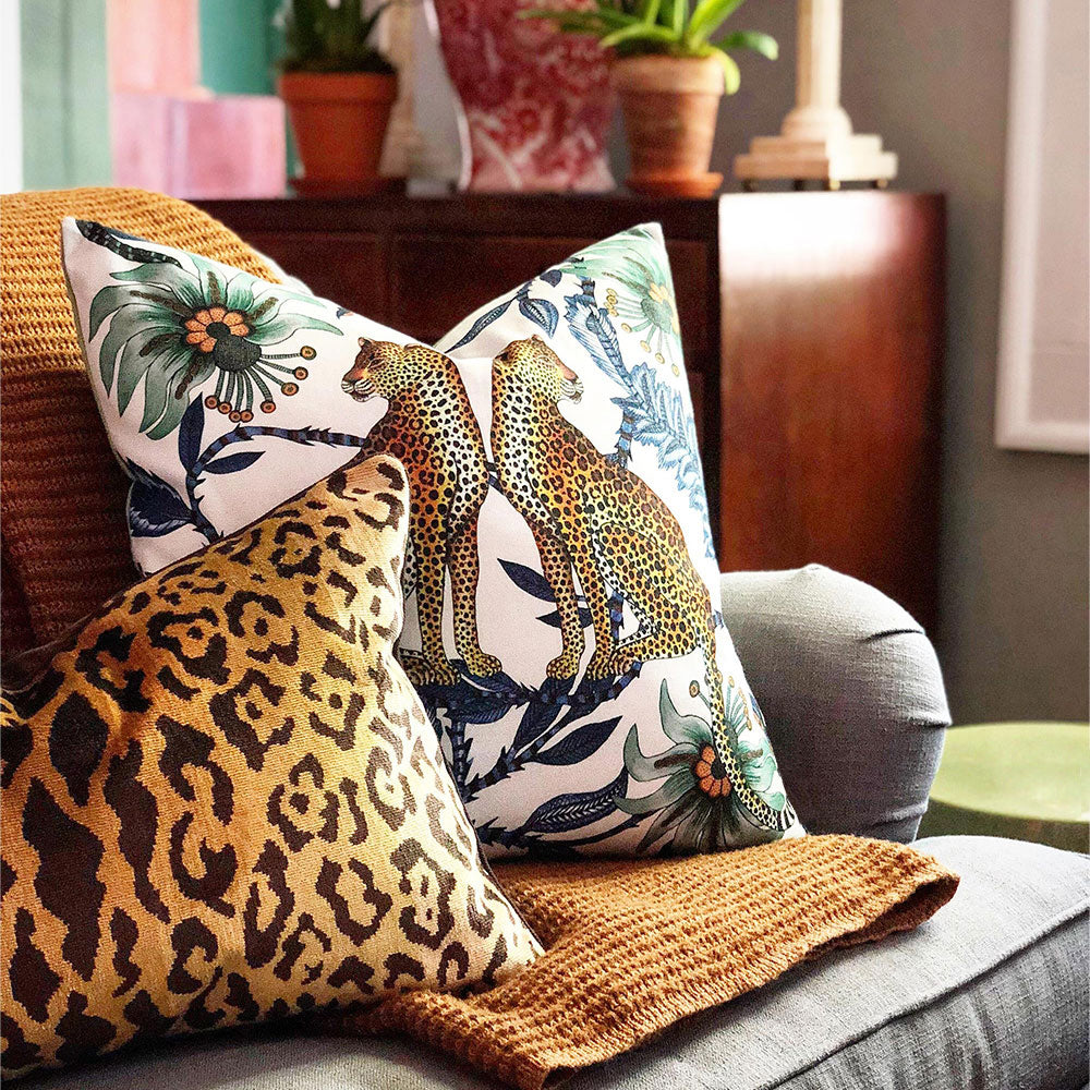 Lifestyle view of the Lovebird Leopards Pillow styled on a sofa next to a brown leopard-print cushion and a knitted throw blanket.