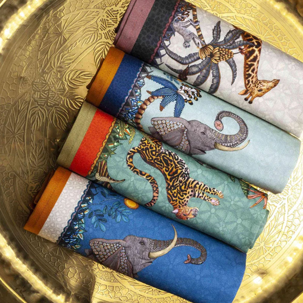 Assorted Sabie Forest Napkins in coordinated colorways arranged inside a decorative gold tray, featuring elephants, giraffes, tiger, and tropical botanical designs.