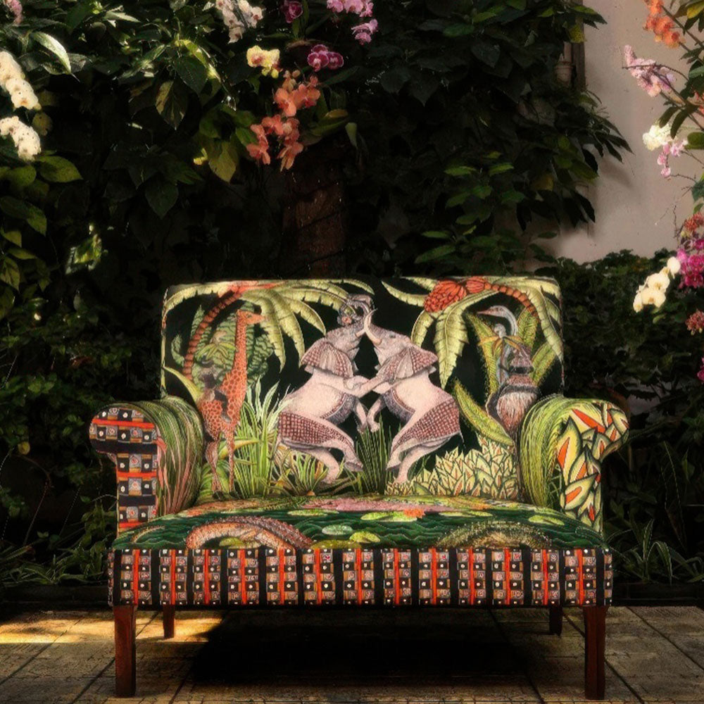 Front view of the Sabie Sofa styled in a lush outdoor courtyard surrounded by vibrant tropical plants and blooming flowers.