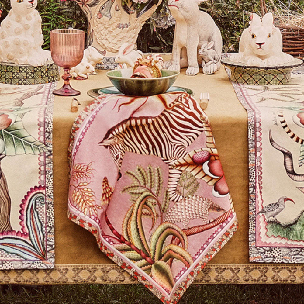 Thanda Stripe Napkins styled on a decorative dining table with zebra and botanical designs in pink, green, cream, and coral tones alongside tableware and sculptural decor.