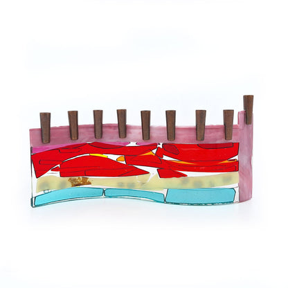 Back view of a handmade fused glass menorah featuring layered pink, red, orange, cream, and aqua glass with decorative blue accents and nine dark metal candle holders on a white background.