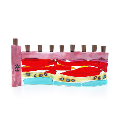 Handmade fused glass menorah featuring layered pink, red, orange, cream, and aqua glass with decorative blue accents and nine dark metal candle holders on a white background.
