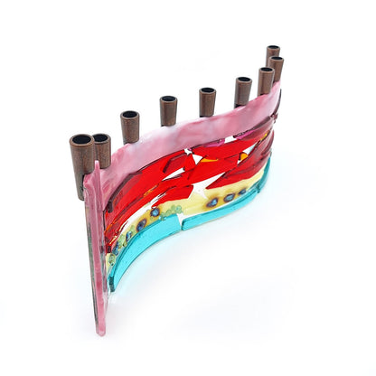 Side view of a handmade fused glass menorah featuring layered pink, red, orange, cream, and aqua glass with decorative blue accents and nine dark metal candle holders on a white background.