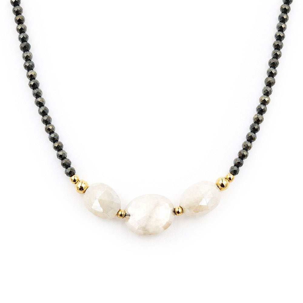 Close-up of a centered necklace featuring faceted dark pyrite beads, three pale peach moonstone beads, and polished gold-tone accents on a white background.
