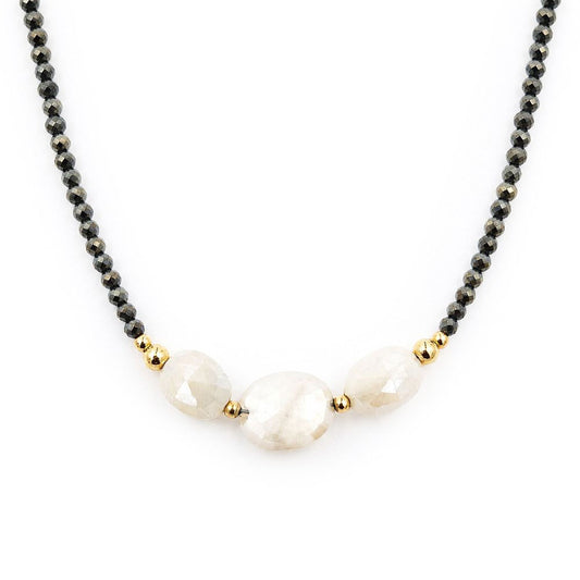 Close-up of a centered necklace featuring faceted dark pyrite beads, three pale peach moonstone beads, and polished gold-tone accents on a white background.