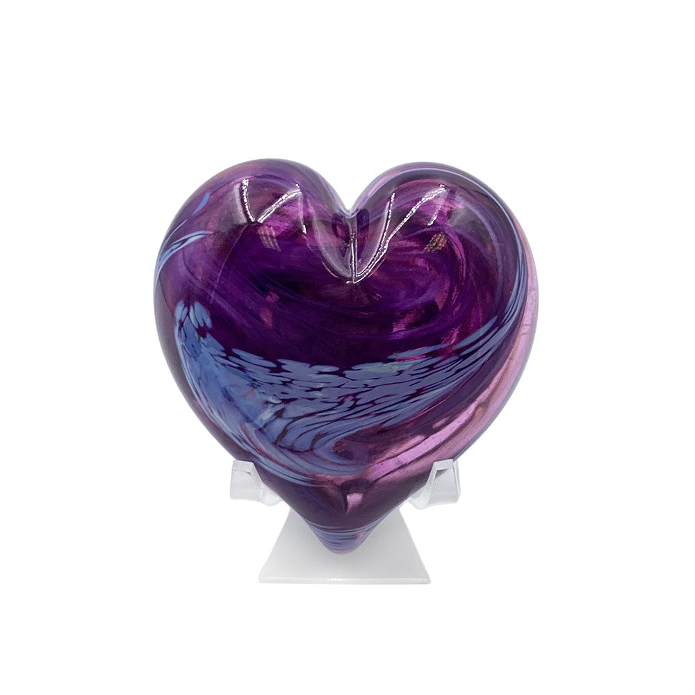 Translucent purple heart-shaped glass sculpture with swirling violet and blue tones, displayed upright on a clear stand against a white background.