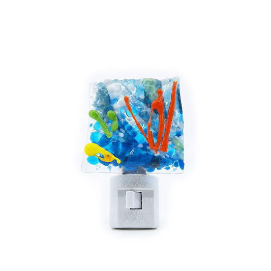 Front view of a handmade coral reef nightlight featuring a square fused glass panel with layered blue glass, bright orange coral-like accents, green and yellow details, and a white plug-in base.