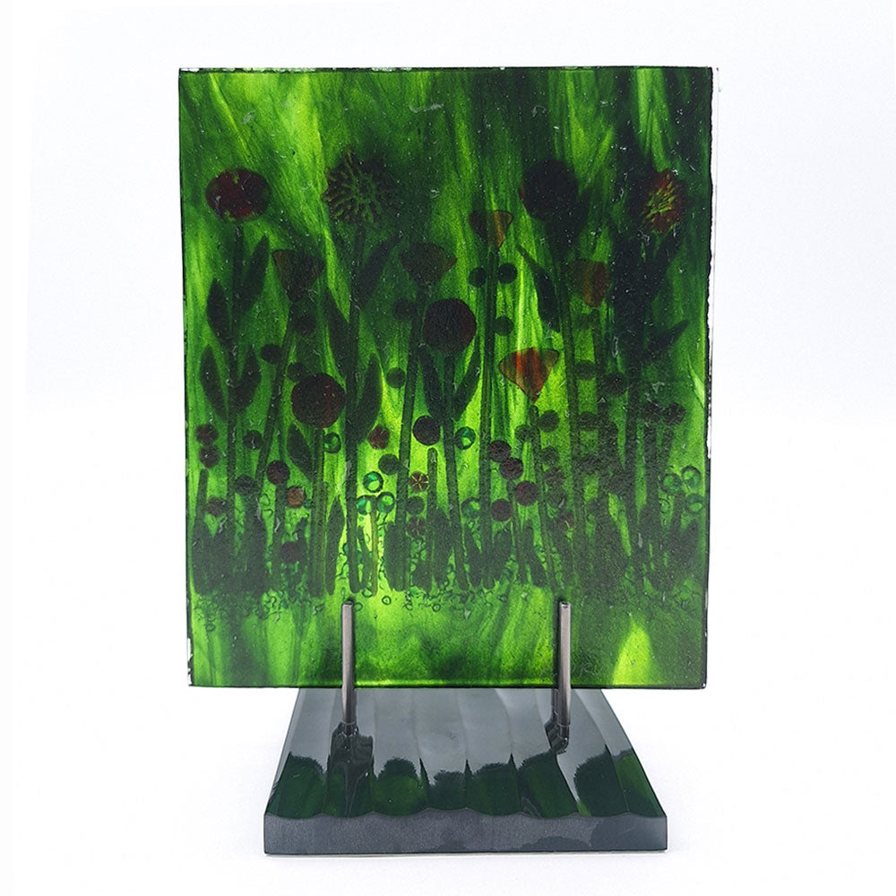 Back view of the Red Roses Panel, a fused glass art piece featuring red and orange flowers against a swirling green background, mounted on a dark green base. 