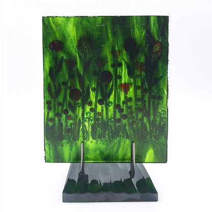 Back view of the Red Roses Panel, a fused glass art piece featuring red and orange flowers against a swirling green background, mounted on a dark green base. 