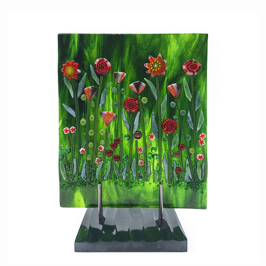 Front view of the Red Roses Panel, a fused glass art piece featuring red and orange flowers against a swirling green background, mounted on a dark green base. 