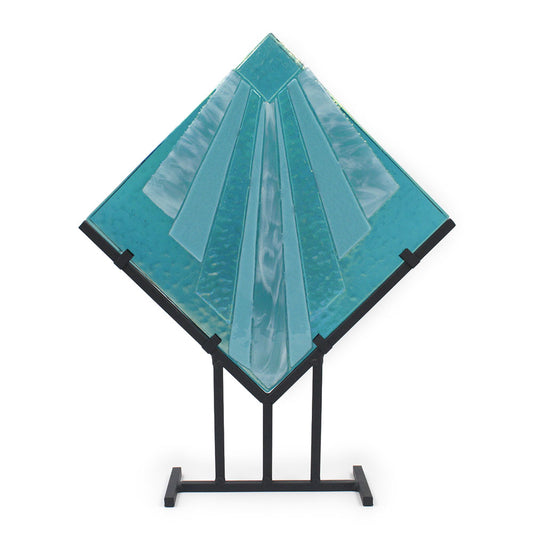 Abstract turquoise glass sculpture with layered geometric panels arranged in a diamond shape, displayed on a black metal stand against a white background.