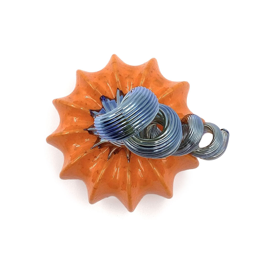 Top view of an orange glass pumpkin showing its deeply ribbed shape and sculptural silver-blue spiral stem.