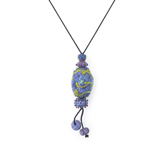Handmade pendant necklace featuring a black cord, layered purple and blue lampwork glass beads, floral and vine details, and two dangling lavender bead accents on a white background.