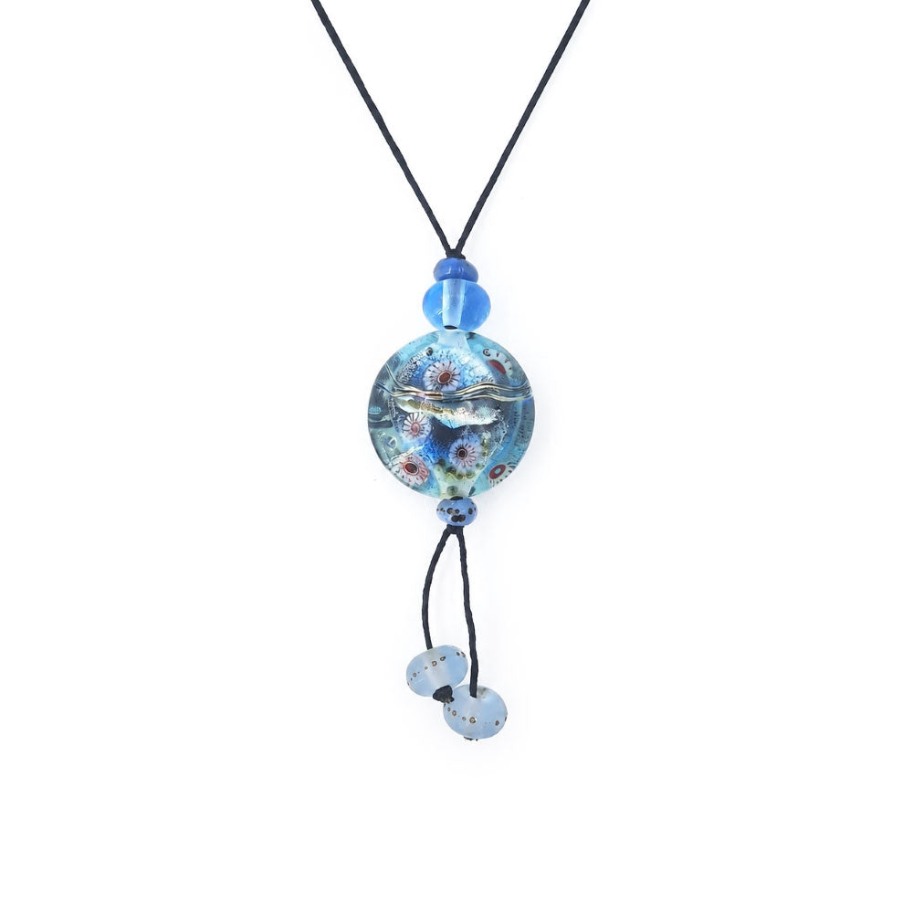 Close-up of a black cord necklace featuring a round aqua-blue glass pendant with raised silver-tone and multicolored details, blue accent beads, and two dangling pale blue glass beads.