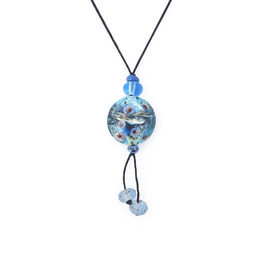 Close-up of a black cord necklace featuring a round aqua-blue glass pendant with raised silver-tone and multicolored details, blue accent beads, and two dangling pale blue glass beads.