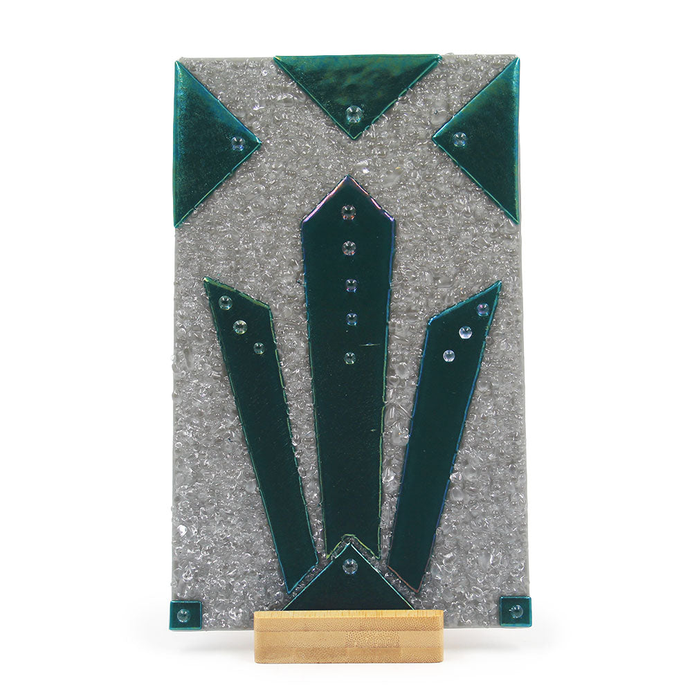 Front view of an abstract glass sculpture featuring a textured silver rectangular panel with layered iridescent teal and green geometric glass elements, small metallic accents, and a light wood display base.