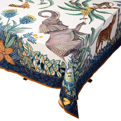 Close-up of an Ardmore wildlife tablecloth draped over a table, showing elephants, a giraffe, tropical plants, and an ornate blue border.