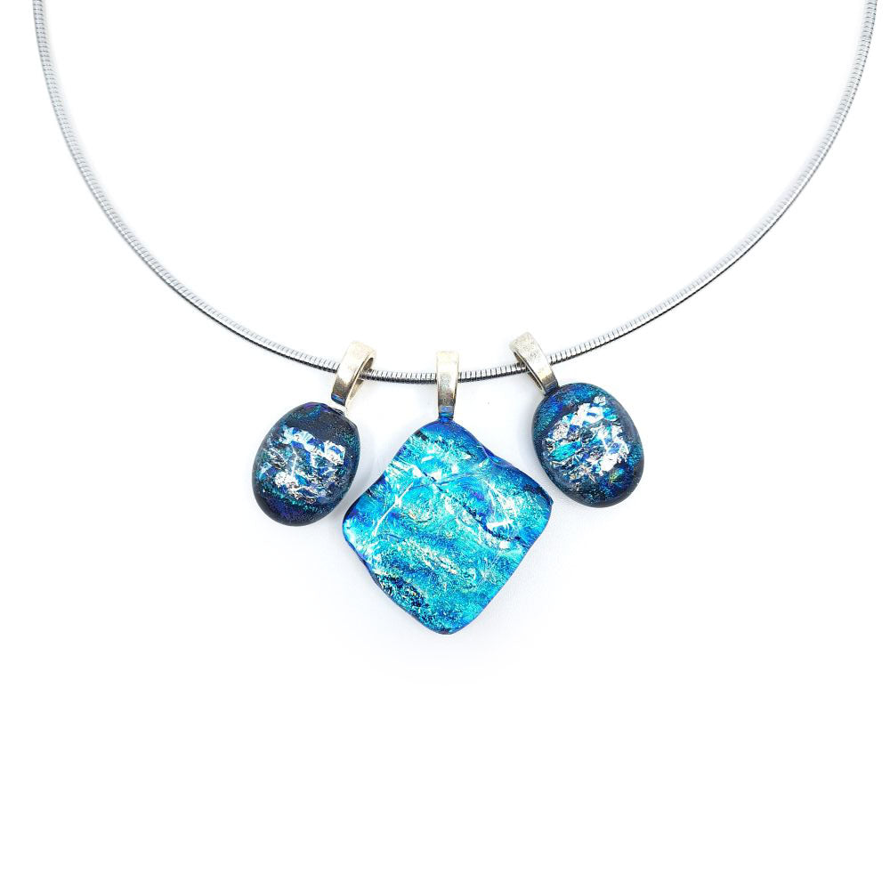 Close-up of a stainless steel necklace featuring three blue dichroic glass charms suspended from sterling silver pinch bails, with a large square center charm flanked by two smaller oval charms.