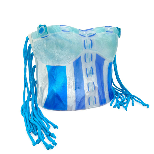 Angled view of a handmade fused glass corset sculpture in pale aqua, turquoise, cobalt blue, and clear glass with long bright blue cord fringe extending from both sides.