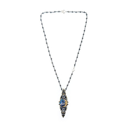 Full view of an ornate necklace featuring a dark beaded chain and an elongated antique gold-tone and black filigree pendant with painted blue metal in the center.