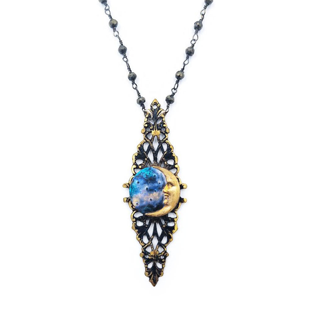 Close-up of an ornate pendant necklace featuring painted blue metal framed by antique gold-tone and dark metal filigree with small bead accents.