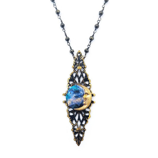 Close-up of an ornate pendant necklace featuring painted blue metal framed by antique gold-tone and dark metal filigree with small bead accents.