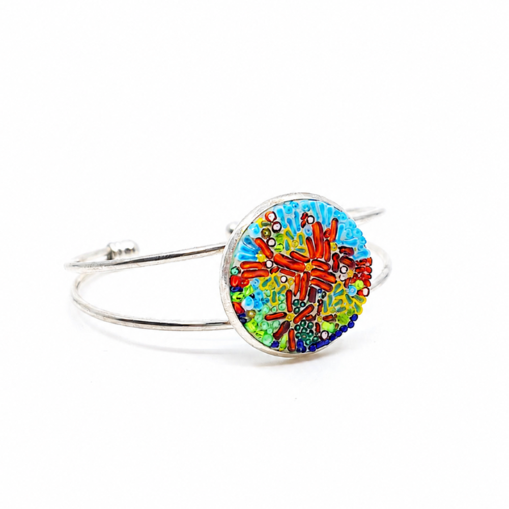 Coral abstract bangle bracelet with a round glass centerpiece in blue, green, brown, and multicolored details on a metal bangle.