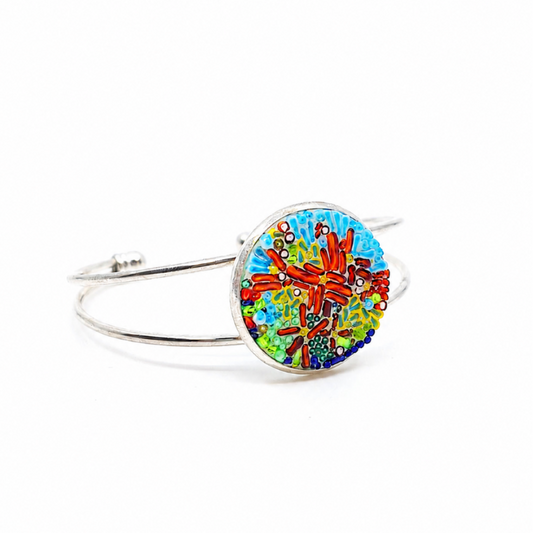 Coral abstract bangle bracelet with a round glass centerpiece in blue, green, brown, and multicolored details on a metal bangle.