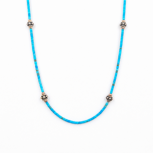 Close-up of a straightened turquoise beaded necklace featuring tiny rectangular beads and four evenly spaced silver-tone floral accents on a white background.