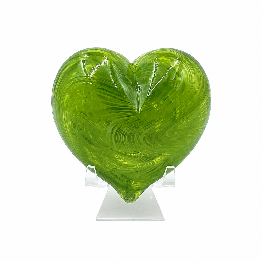 Translucent green heart-shaped glass sculpture with swirling lime and olive tones, displayed upright on a clear stand against a white background.