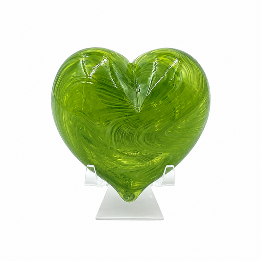 Translucent green heart-shaped glass sculpture with swirling lime and olive tones, displayed upright on a clear stand against a white background.