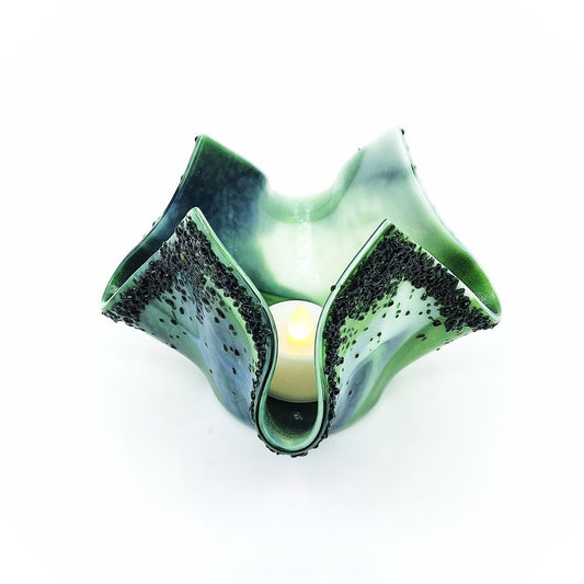 Handmade green and white glass tulip candle holder shown with a glowing candle inside, featuring sculpted asymmetrical petals and textured dark green accents.