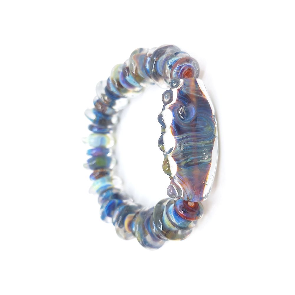 Handmade glass bead bracelet featuring translucent blue, purple, amber, and iridescent tones with a large curved focal bead at the center, photographed on a white background.