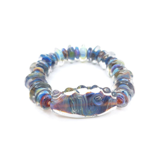 Handmade glass bead bracelet featuring translucent blue, purple, amber, and iridescent tones with a large curved focal bead at the center, photographed on a white background.