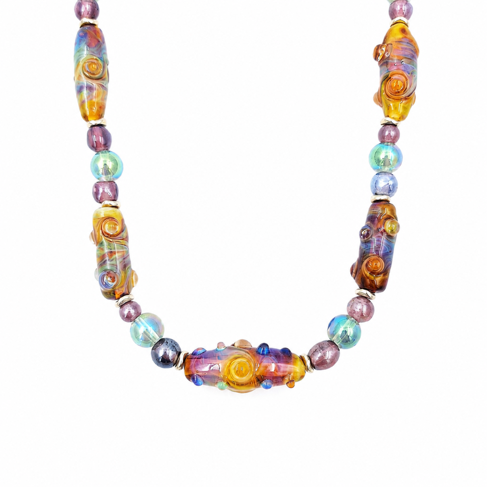 Close-up of a colorful glass bead necklace featuring elongated amber, purple, and blue beads with raised spiral details, accented by round iridescent beads and silver-tone spacers.