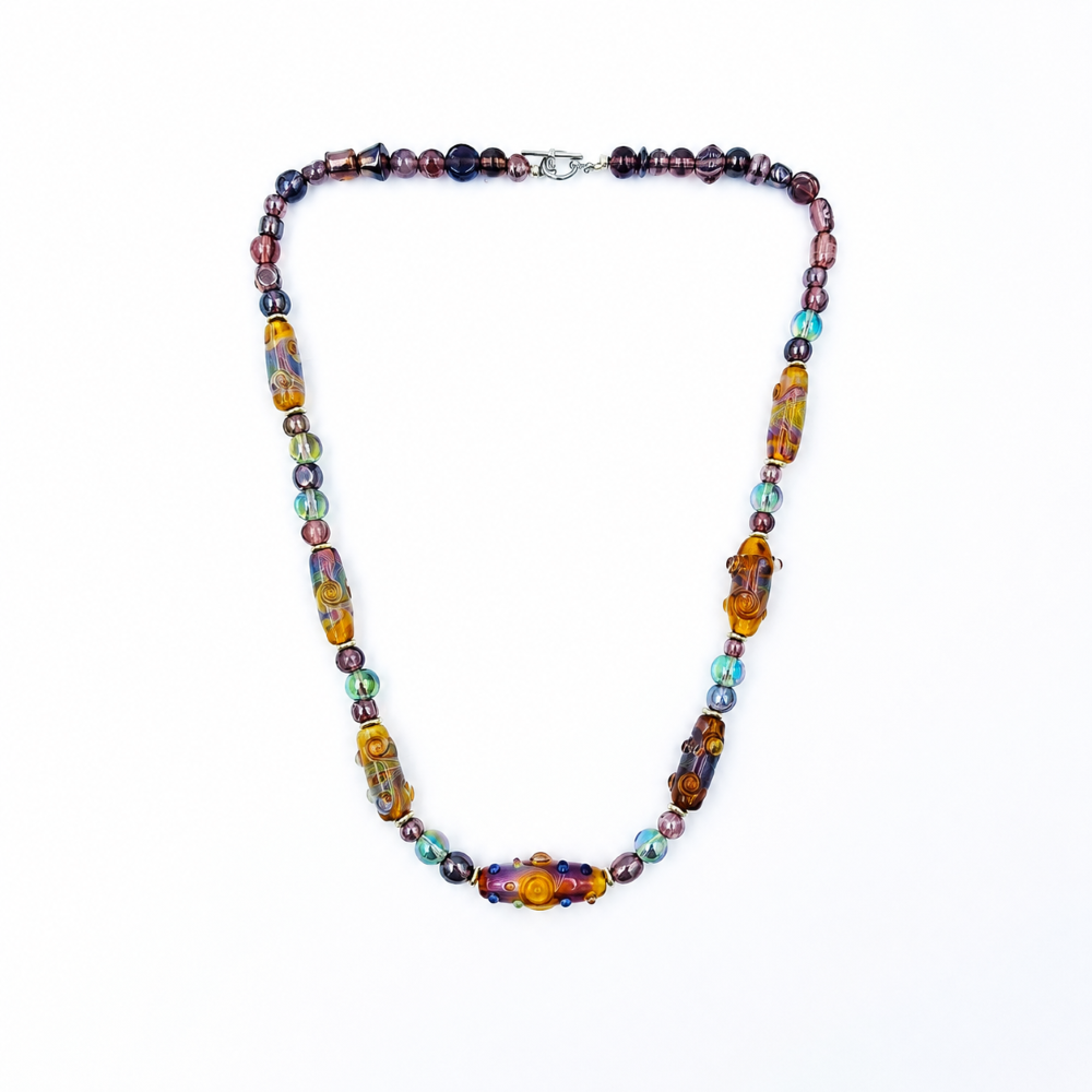 Full view of a multicolored glass bead necklace arranged in a rounded triangular shape, featuring purple and iridescent round beads, elongated spiral-patterned beads, and a silver-tone clasp.