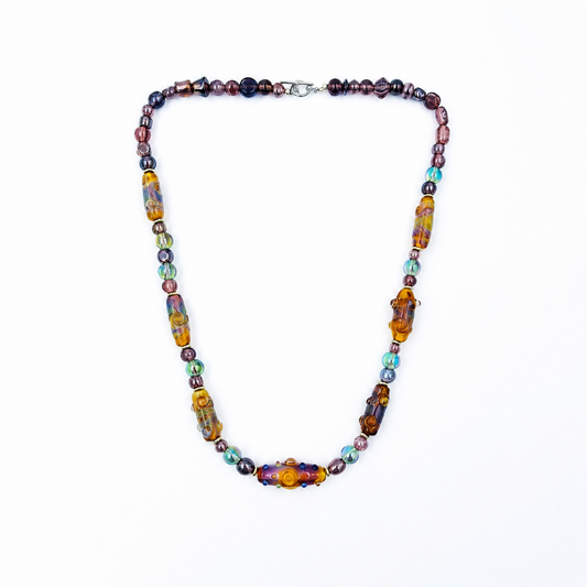 Full view of a multicolored glass bead necklace arranged in a rounded triangular shape, featuring purple and iridescent round beads, elongated spiral-patterned beads, and a silver-tone clasp.