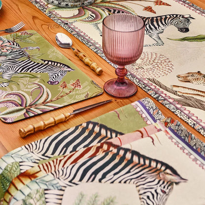 Ardmore wildlife table runner styled on a wooden dining table with zebra-patterned linens, bamboo-handled flatware, and a pink glass goblet.