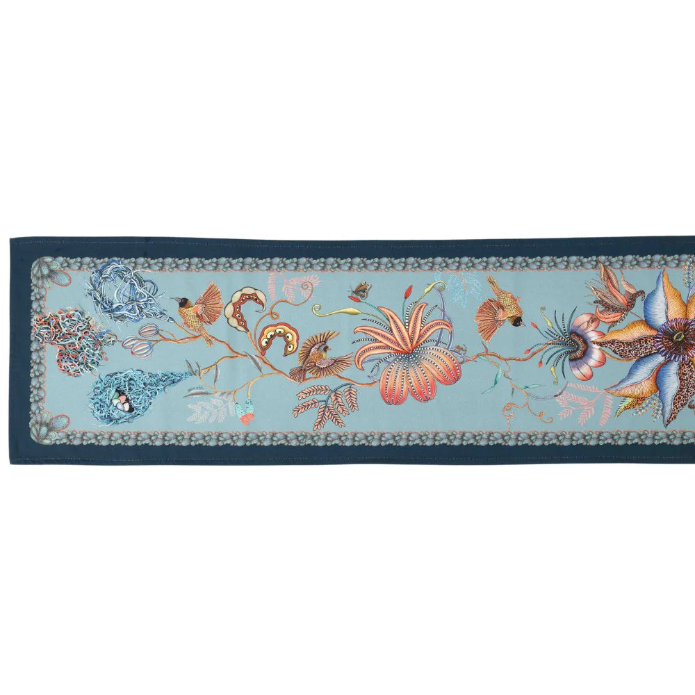 Full-length mist blue Thanda Nest table runner with birds, flowers, foliage, and woven nest details.