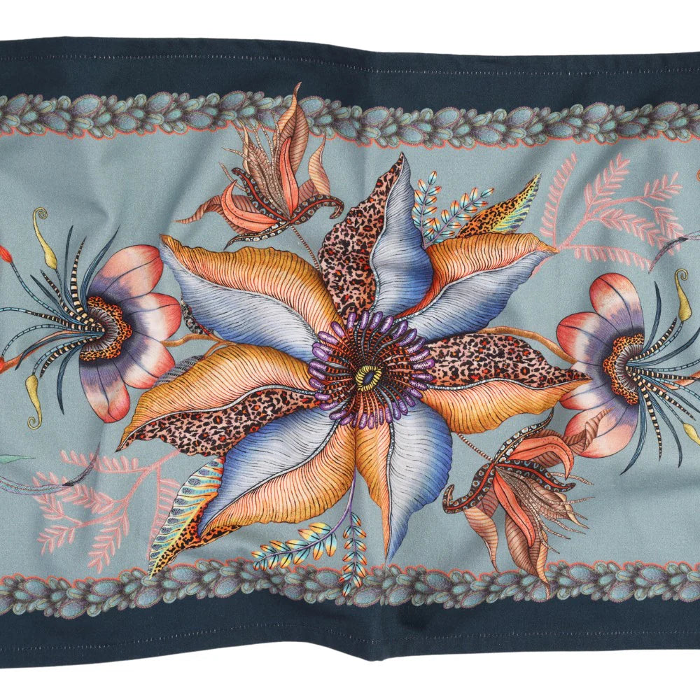 Close-up of mist blue Thanda Nest table runner showing large flowers, birds, foliage, and patterned border.