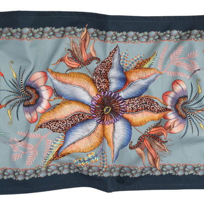 Close-up of mist blue Thanda Nest table runner showing large flowers, birds, foliage, and patterned border.
