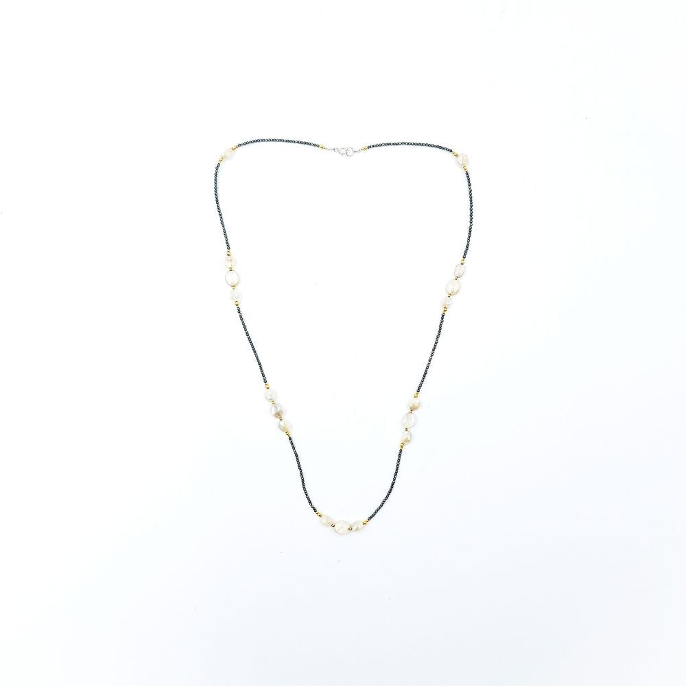 Long necklace featuring tiny dark pyrite beads, peach moonstone oval beads, small gold-tone accents, and a silver-tone clasp, displayed on a white background.