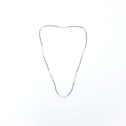 Long necklace featuring tiny dark pyrite beads, peach moonstone oval beads, small gold-tone accents, and a silver-tone clasp, displayed on a white background.