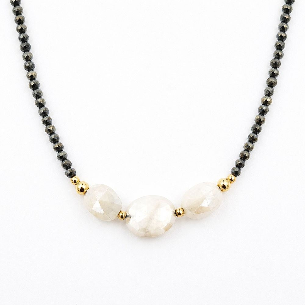 Close-up of a centered necklace featuring faceted dark pyrite beads, three pale peach moonstone beads, and polished gold-tone accents on a white background.