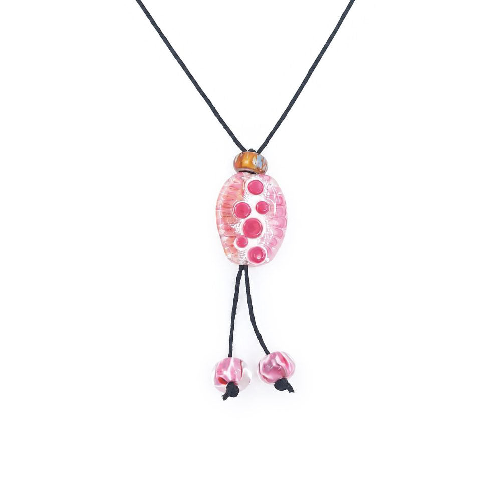 Close-up of a black cord necklace featuring an oval pink glass pendant with raised circular details, an amber accent bead, and two dangling pink glass beads.