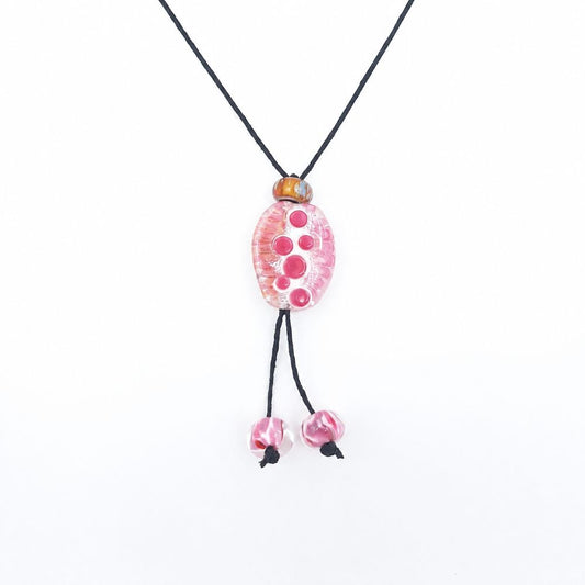 Close-up of a black cord necklace featuring an oval pink glass pendant with raised circular details, an amber accent bead, and two dangling pink glass beads.