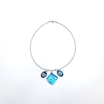 Full view of a stainless steel chain necklace featuring three blue dichroic glass charms with sterling silver pinch bails, including a square center pendant and two smaller oval side charms.